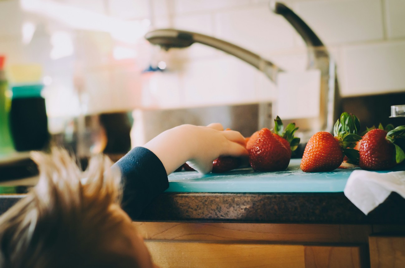 Child grabbing strawberries from the kitchen counter